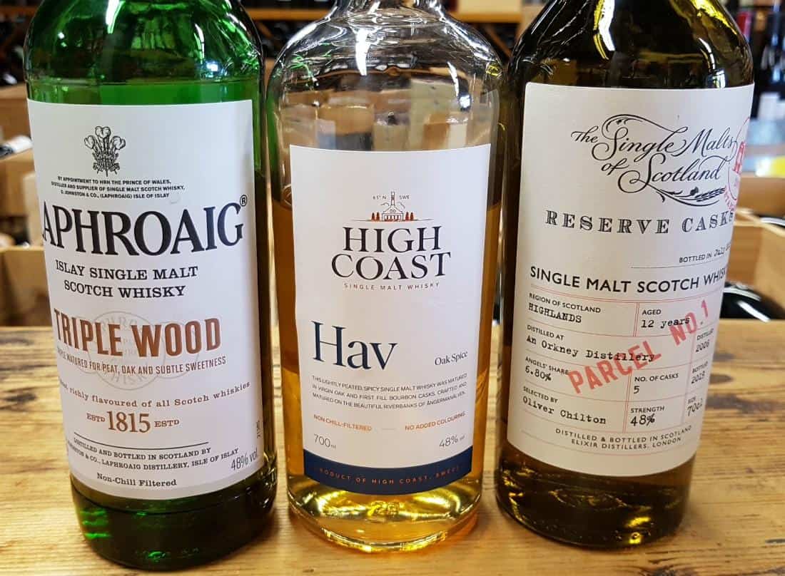 Trois bouteilles de whisky, tourbe à 48 %, sur une table en bois.